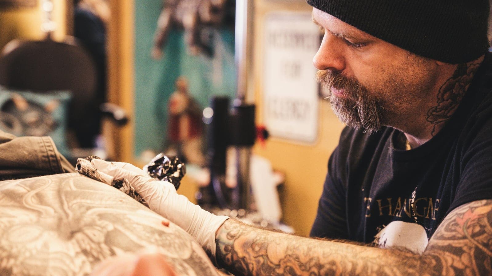 A tattoo artist working on a client's arm in a studio, machine in hand