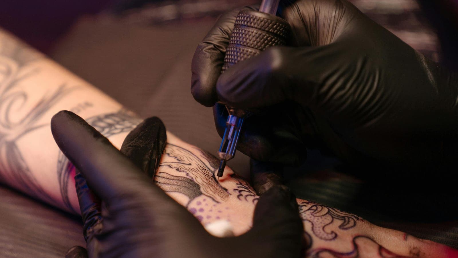 Close-up of a tattoo artist working line work on a client's arm