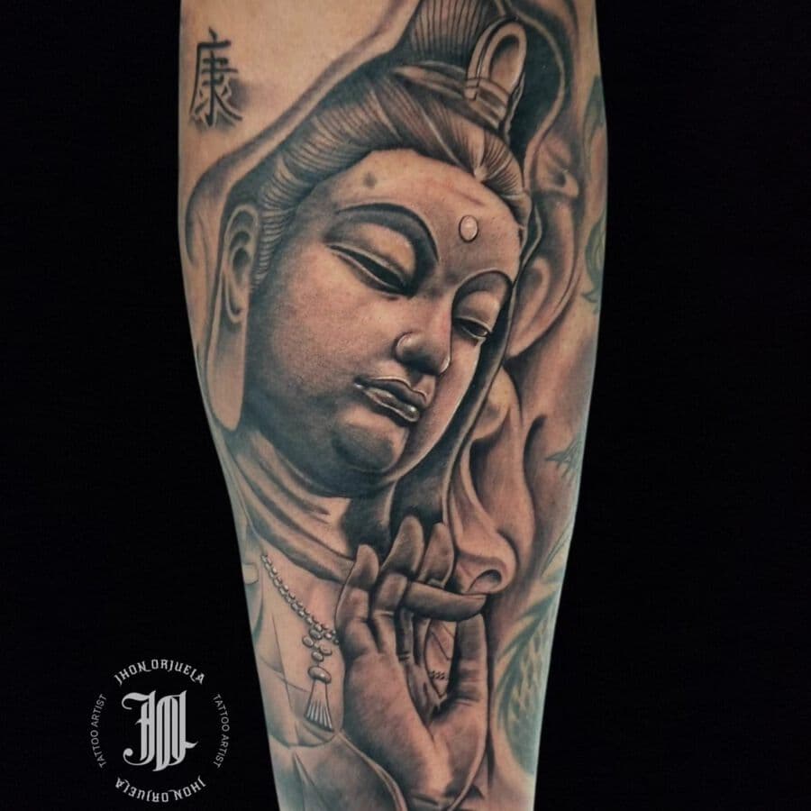 Black and grey Buddhist figure tattoo on a forearm, from the Aura Tattoo & Meaning gallery