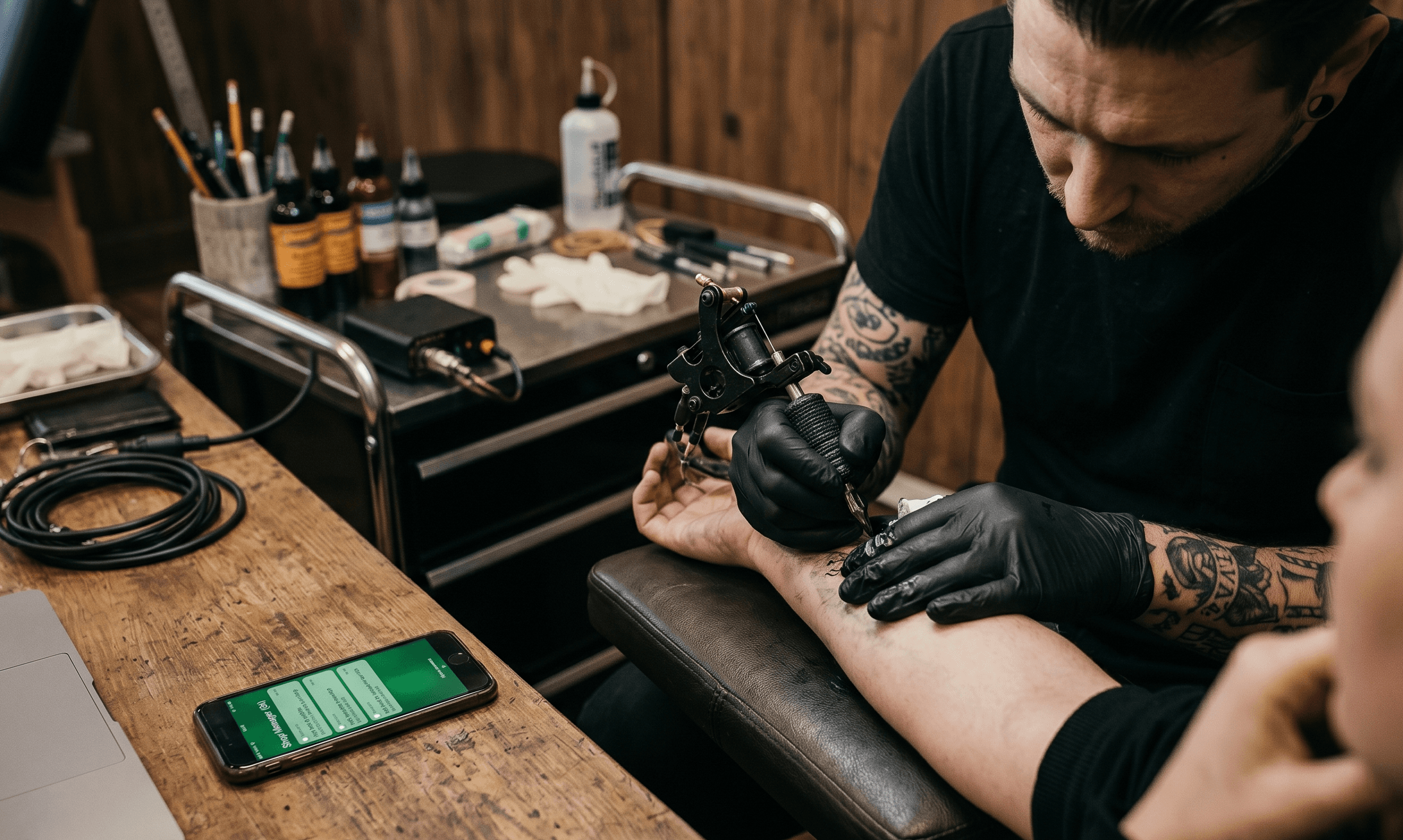 Tatuador à secretária com computador e telefone perdido na administração em vez de tatuar